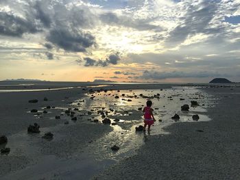 Rear view of baby girl walking on beach against sky during sunset