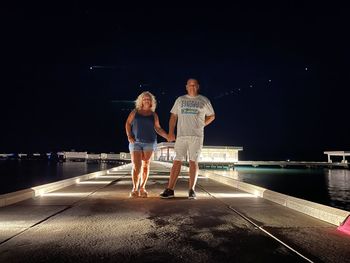 Full length of young woman standing in swimming pool at night