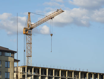 Low angle view of crane by building against sky