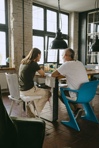 Male and female business colleagues discussing over laptop while sitting on chair in studio