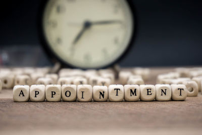 Close-up of appointment text made with toy blocks against alarm clock on wooden table