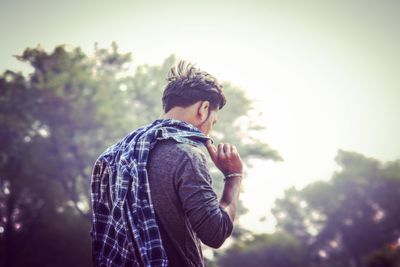 Rear view of man holding shirt while standing against sky