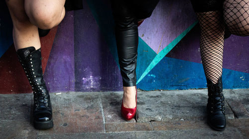 Low section of women in high heels standing against wall