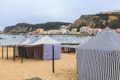 Hooded beach chairs by sea against sky