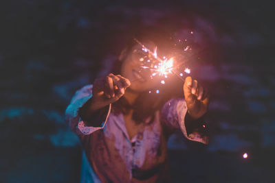 Close-up of hand holding illuminated fireworks against sky at night