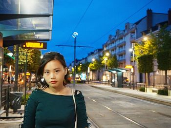 Portrait of young woman standing roadside at dusk