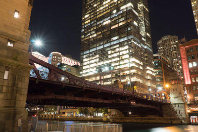 Low angle view of illuminated bridge and buildings at night
