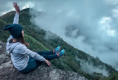 Full length of carefree young woman sitting on cliff during foggy weather