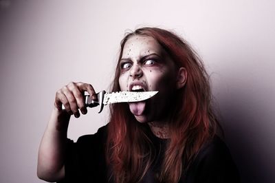 Spooky young woman with knife against gray background