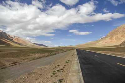 A flat, newly built wide asphalt road leads to the beautiful mountains in the distance