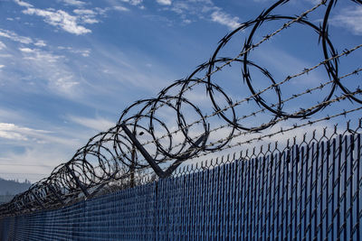 Low angle view of barbed wire fence against sky