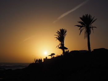 Silhouette palm trees on beach against sky during sunset