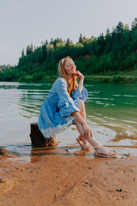 Woman sitting on shore at beach against sky