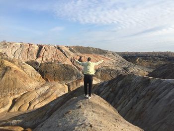 Rear view of woman standing on rock against sky