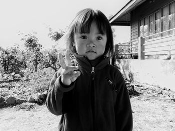 Cute girl gesturing peace sign while looking away outdoors