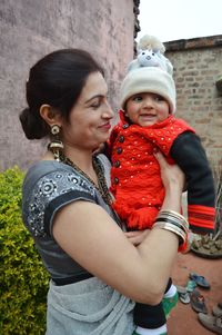 Smiling woman holding baby girl against houses