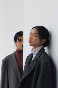 Young woman looking at friend with eyes closed standing against wall