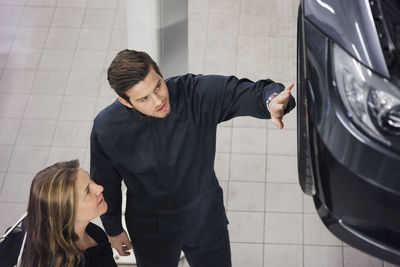 High angle view of young mechanic explaining to female customer at shop