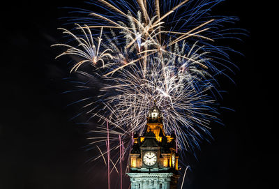 Low angle view of illuminated clock tower and firework display at night