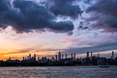 Sea by modern buildings against sky during sunset