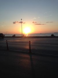 Street by sea against sky during sunset