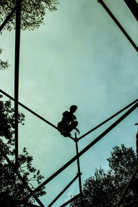 Low angle view of silhouette man hanging on rope against sky