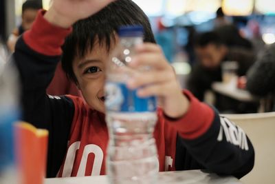 Close-up portrait of smiling man holding water bottle while sitting at restaurant table