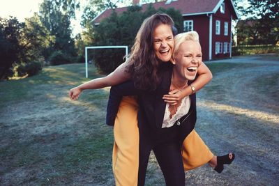 Cheerful woman piggybacking female friend on field