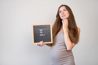 Young woman using digital tablet while standing against wall