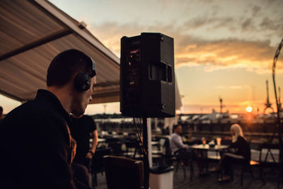 Man sitting at restaurant against sky during sunset