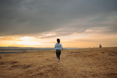Rear view of woman walking at beach against sky during sunset