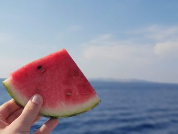 Cropped image of hand holding apple against sky