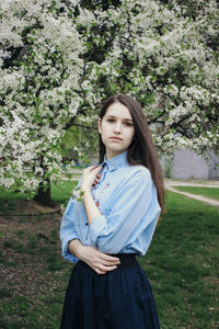 Portrait of beautiful young woman standing against tree