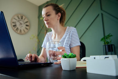 Woman holds glass of water while works at home workplace
