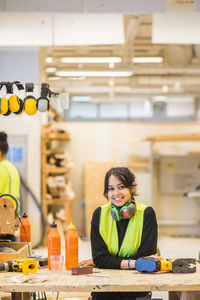 Portrait of smiling young female trainee leaning on workbench at workshop