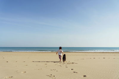 Rear view of girl running with dog towards sea  against sky