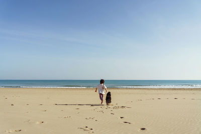 Rear view of woman walking at beach against sky