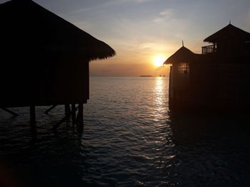 Scenic view of sea and silhouette buildings against sky during sunset