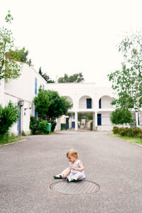 Boy sitting on road by building