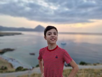 Portrait of smiling boy standing on land against sky