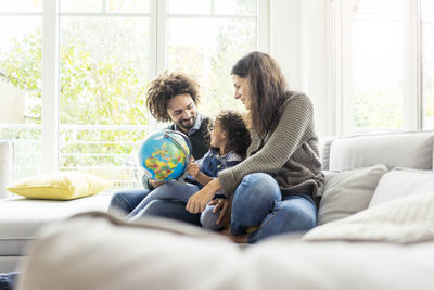 Happy family sitting on couch with globe, daughter learning geography