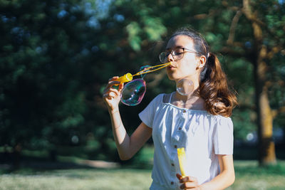 Portrait of a caucasian teenage girl blowing soap bubbles in the park.