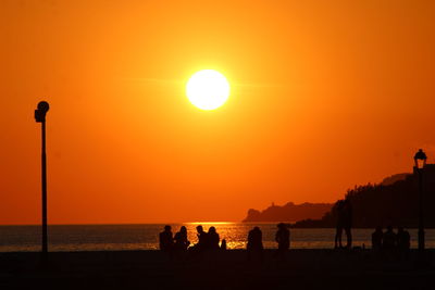 Silhouette people on beach against orange sky