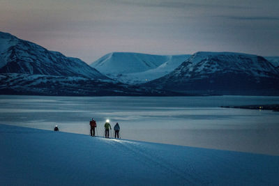 A group of 3 people skis at sunrise with ocean and mountains behind