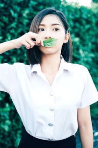 Young woman covering mouth with leaf while standing against plants