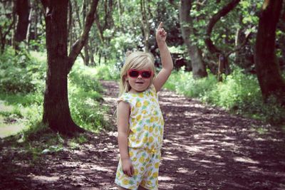 Portrait of girl wearing sunglasses while pointing in forest