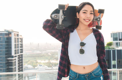 Portrait of smiling young woman photographing with city in background