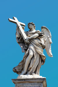 Low angle view of bernini angel sculpture on san angelo bridge in rome, italy, against blue sky