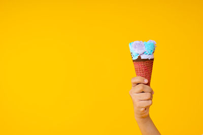Hand holding ice cream cone against yellow background