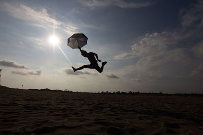 Silhouette man jumping at shore against sky during sunset